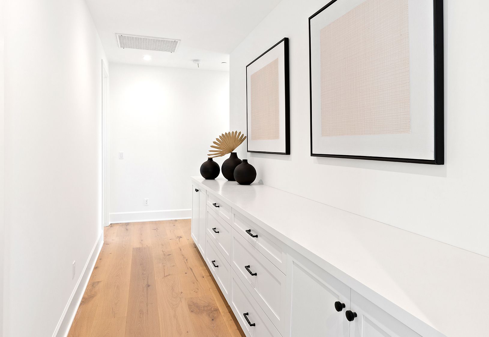 A long hallway with wooden floors and white cabinets.