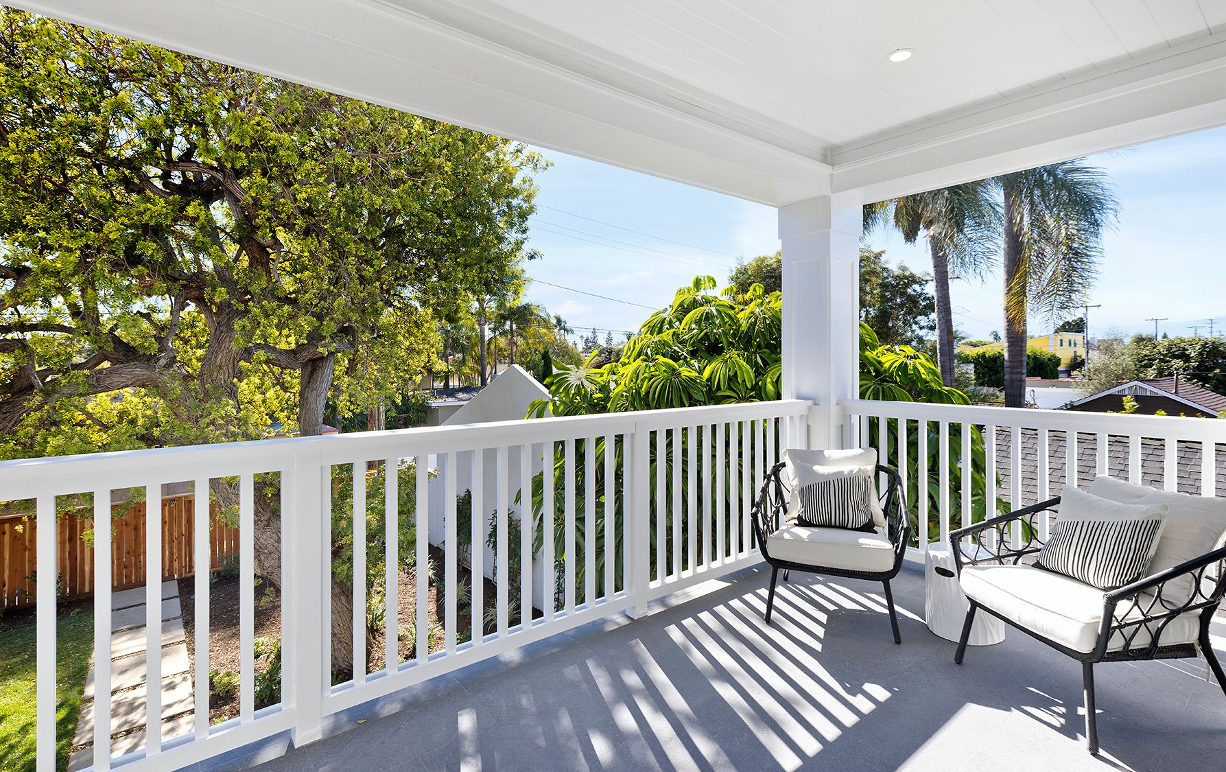 A balcony with a white railing and chairs and trees in the background.