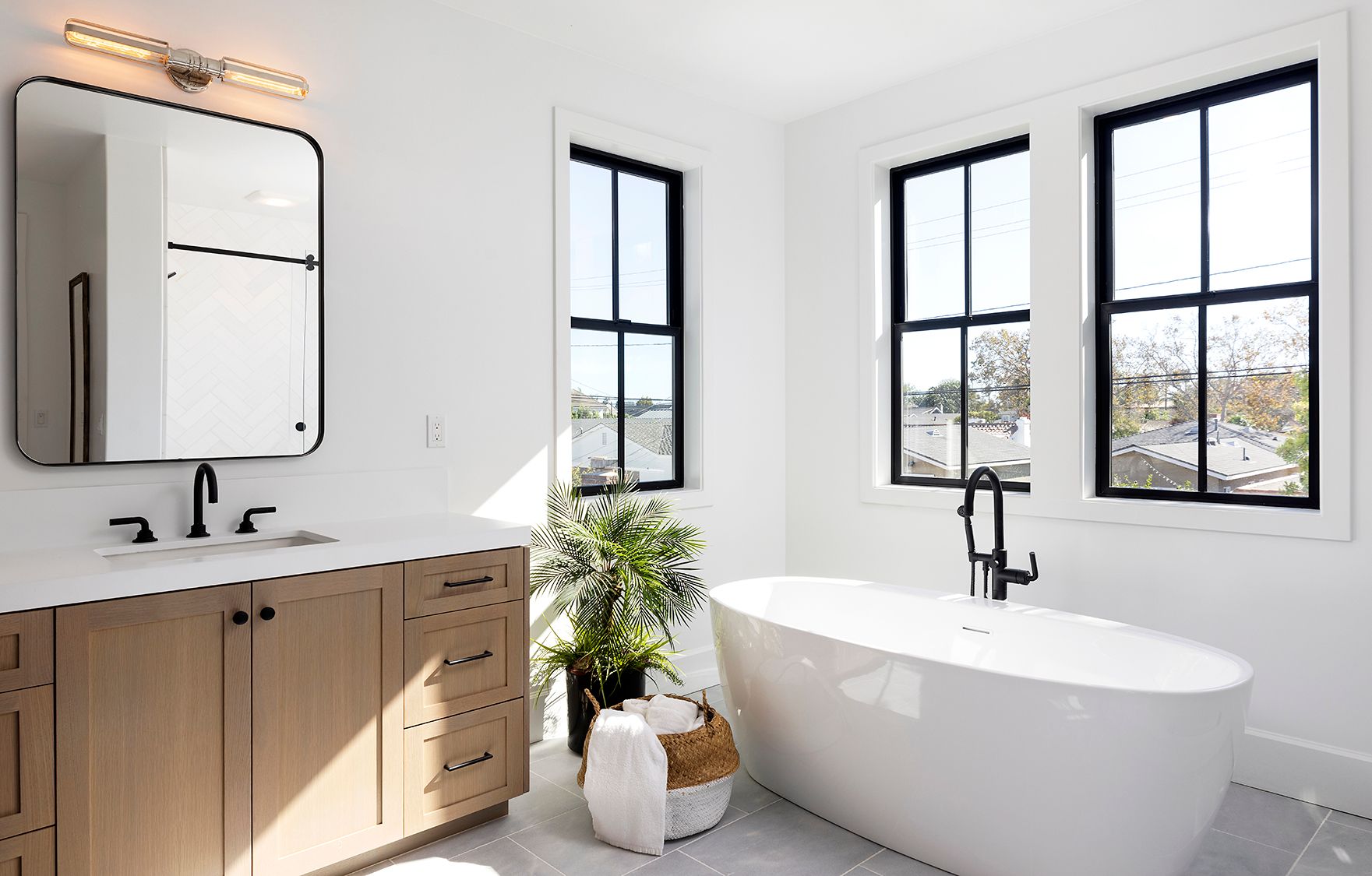 A bathroom with a tub , sink , mirror and two windows.