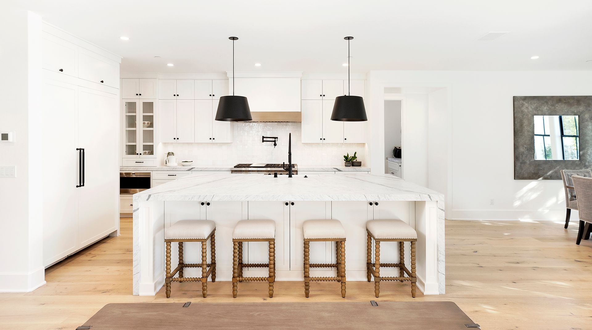 A kitchen with white cabinets and stools and a large island.