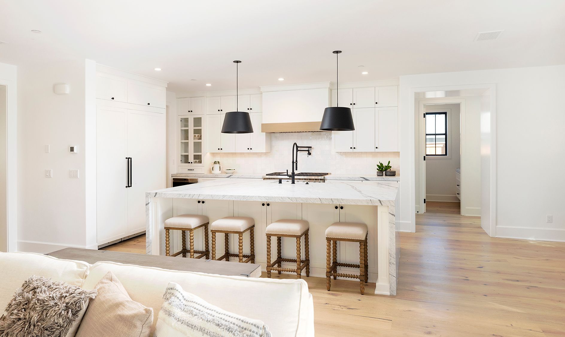 A kitchen with a large island and stools in a living room.