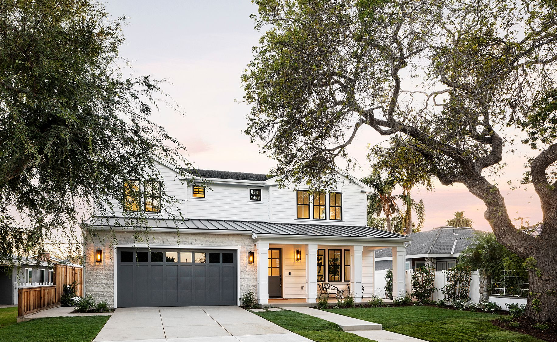 A large white house with a gray garage door is surrounded by trees.