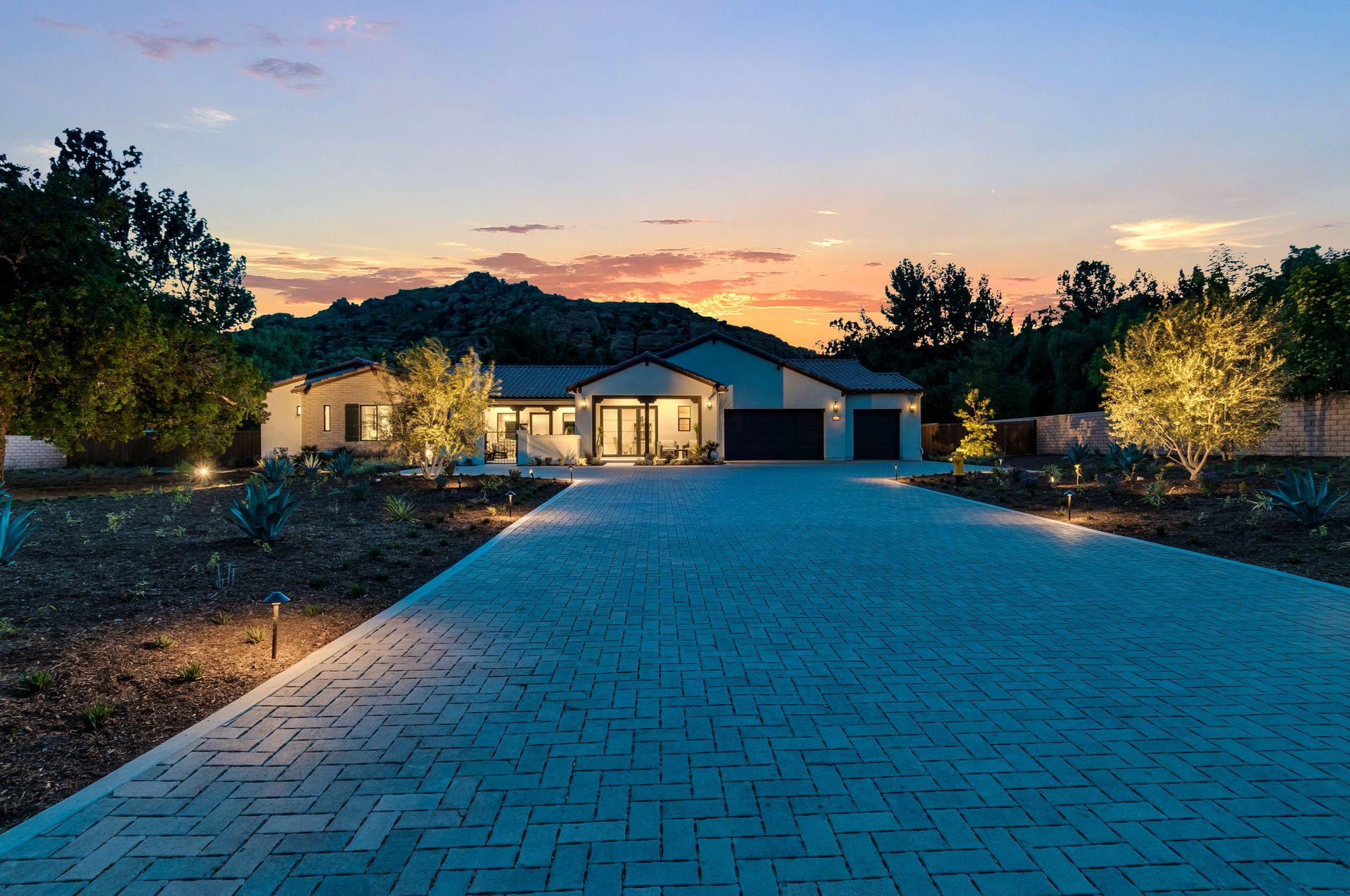 A brick driveway leading to a house with a sunset in the background.