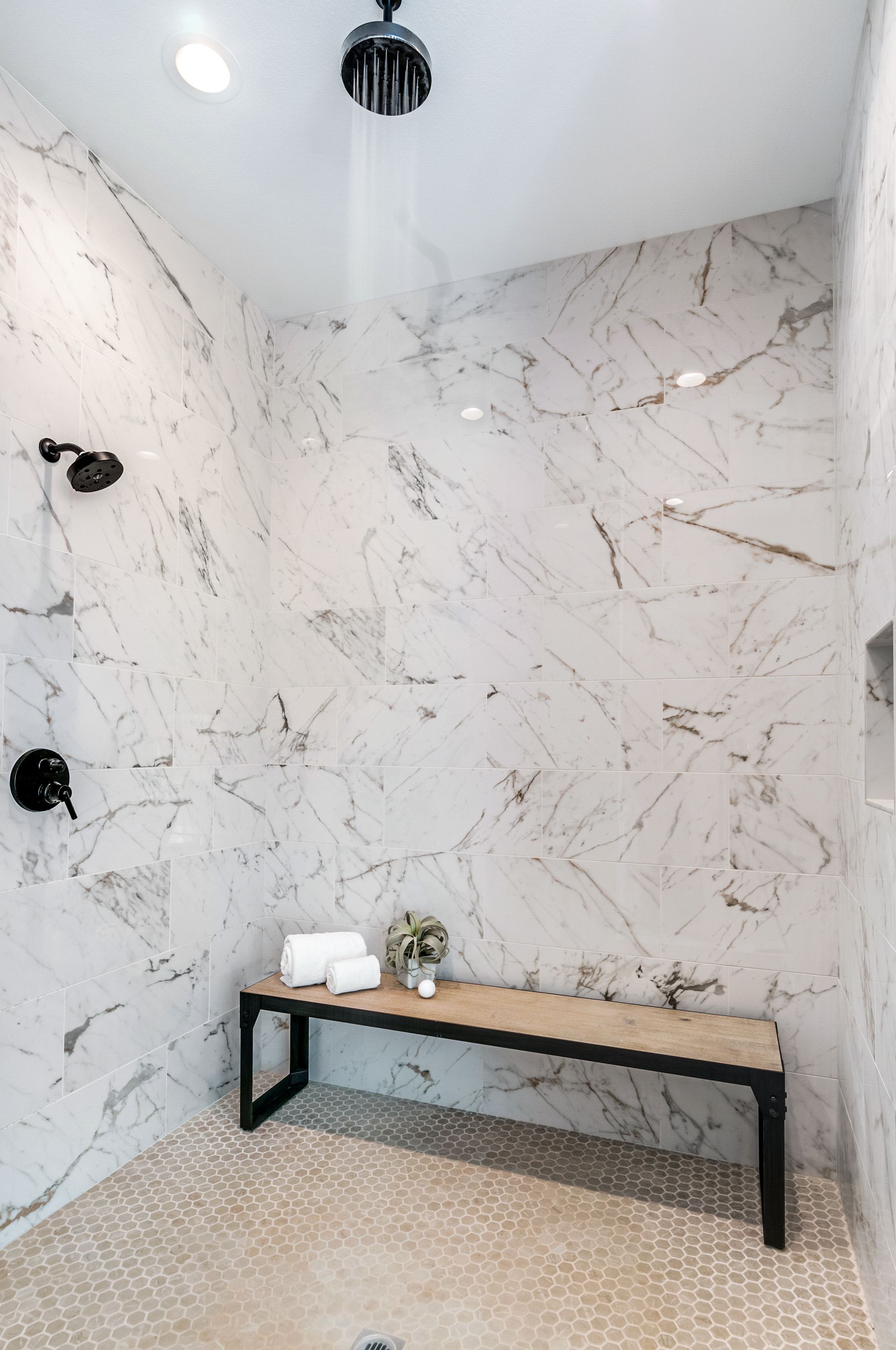 There is a bench in the shower with marble walls.