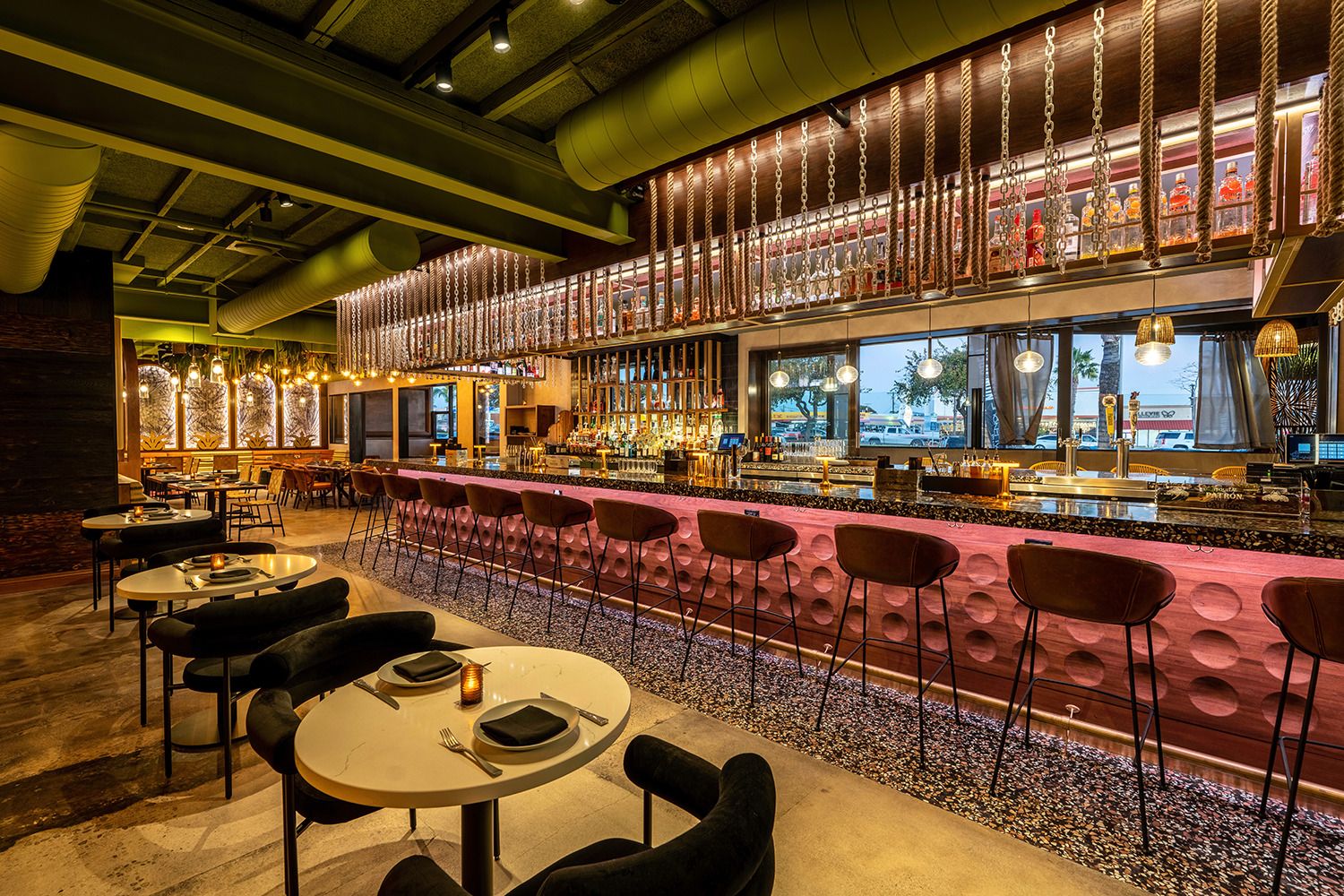 A restaurant with tables and chairs and a long bar.