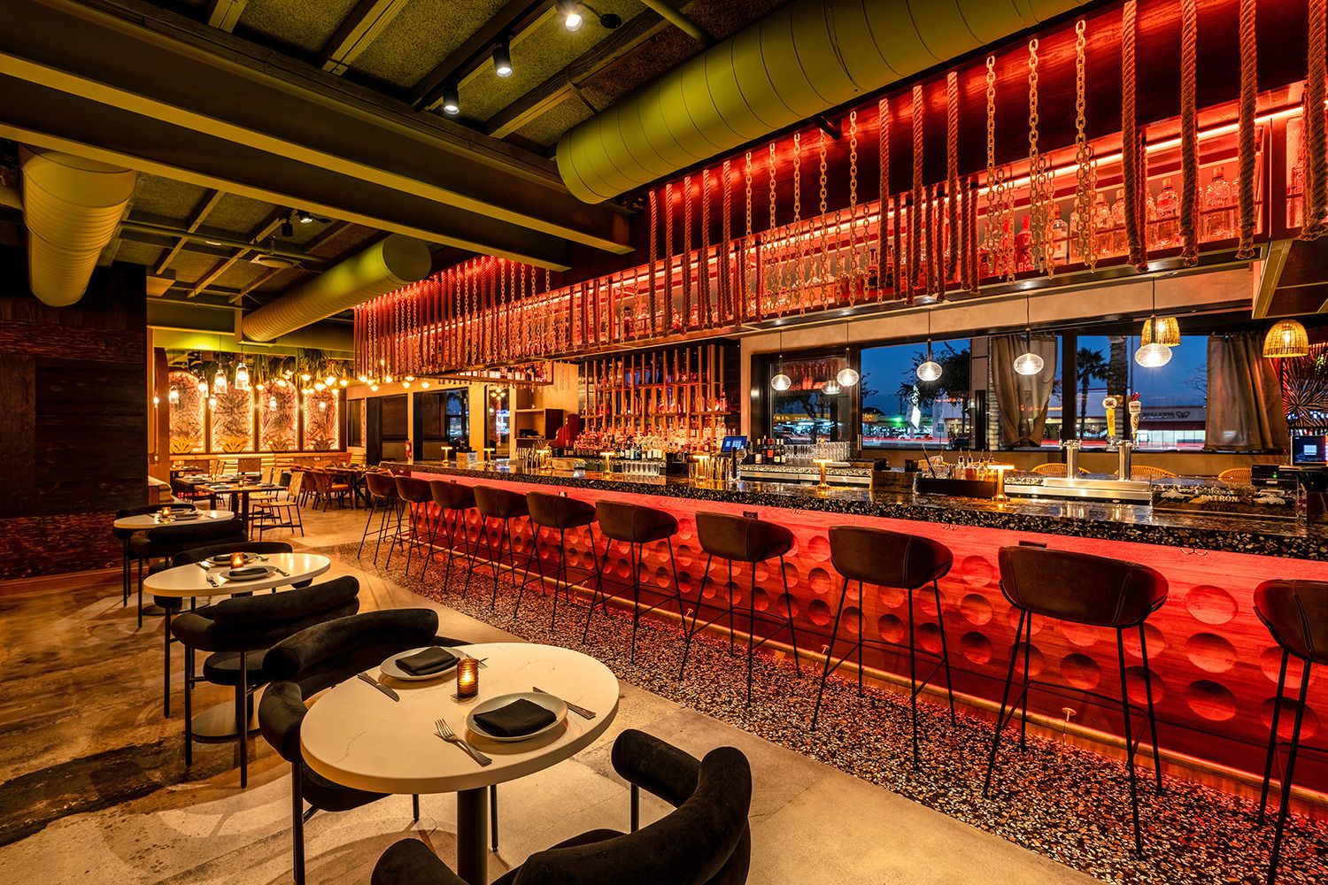 A restaurant with tables and chairs and a long bar.