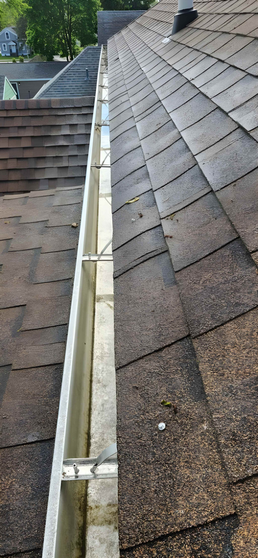 Roof shingles beside a narrow gutter along a house roofline, viewed from above