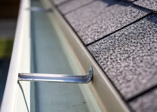 Metal gutter cleaning hook on a roof edge with shingles and gutter.