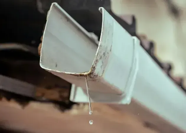Broken white gutter end with a dripping water drop, close-up.