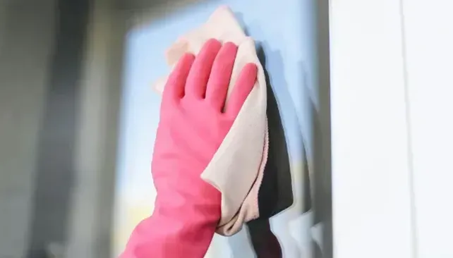 Pink-gloved hand wiping a glass window with a cloth.
