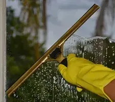 Yellow-gloved hand cleaning a window with a squeegee