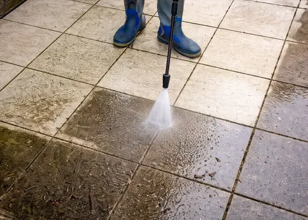 Person pressure-washing a tiled patio with blue boots visible