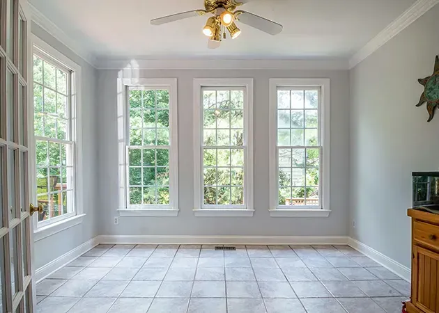 Empty bright room with large windows, gray walls, tiled floor, and a ceiling fan