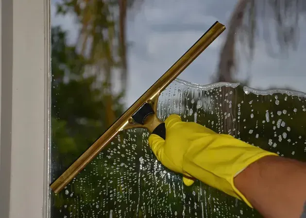 Gloved hand using a squeegee to clean a wet window pane outdoors