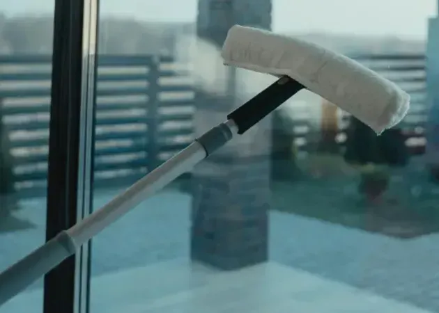 White window squeegee on a handle cleaning a glass window with city buildings blurred behind it