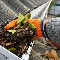 Gloved hand removing leaves and debris from a clogged roof gutter