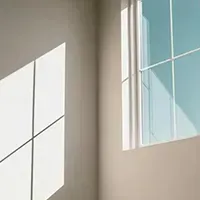 Sunlit empty room corner with gray walls and a blue-tinted window shadow on the wall