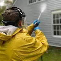 Person in a yellow jacket using a spray nozzle near a house exterior