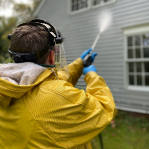 Person in a yellow jacket using a spray nozzle near a house exterior