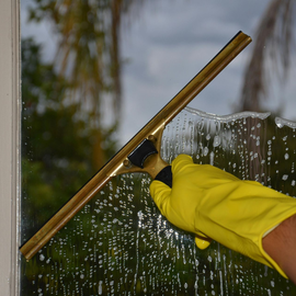 Yellow-gloved hand cleaning a window with a squeegee
