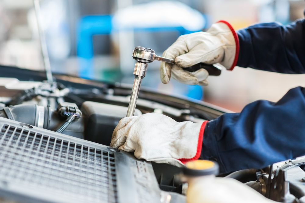 Mechanic in Blue Work Suit and Gloves Using a Wrench on a Car Engine in a Garage — Autopro Taree in Taree, NSW