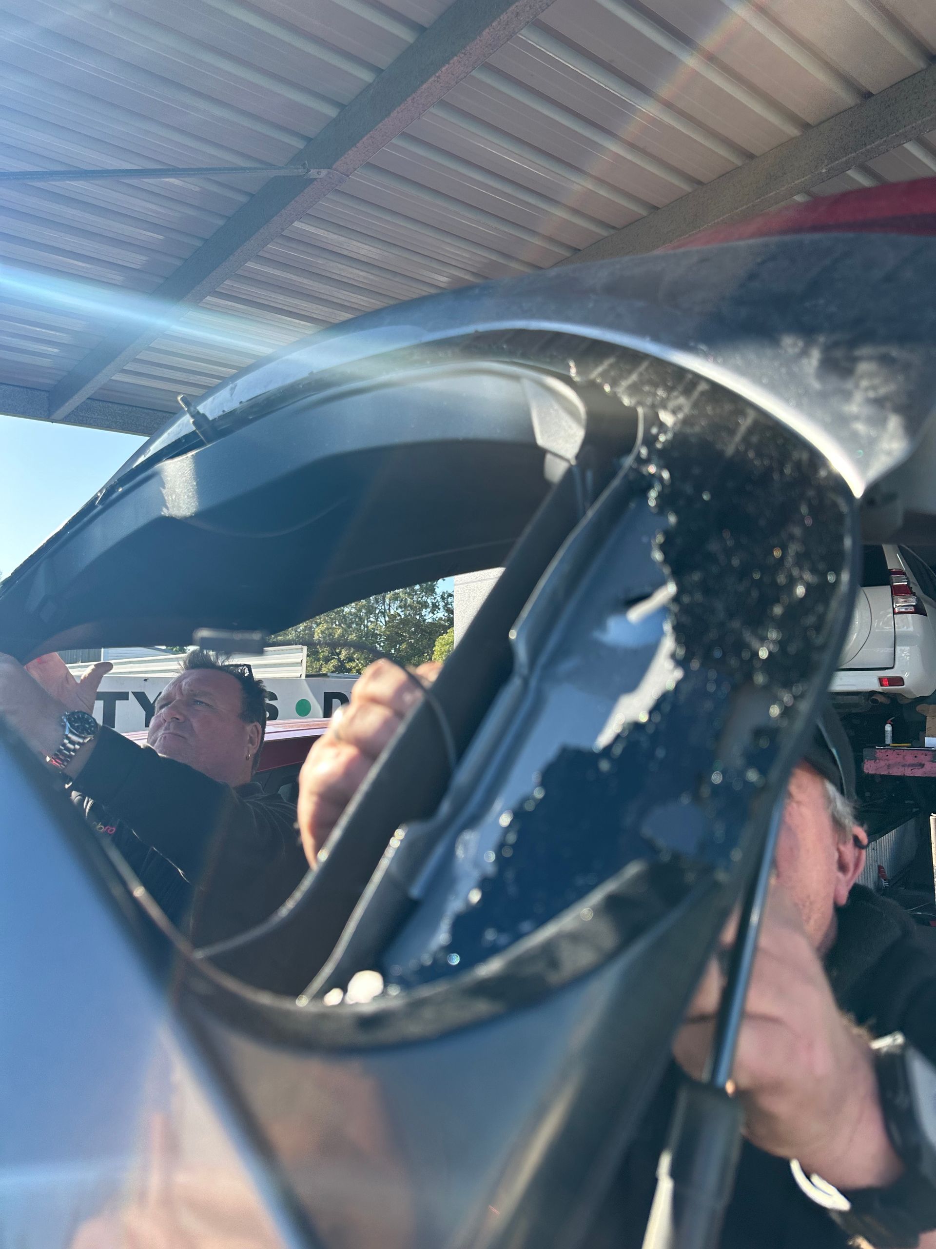 Person Holding a Damaged Windshield Inside a Car Under a Metal Roof — Autopro Taree in Taree, NSW