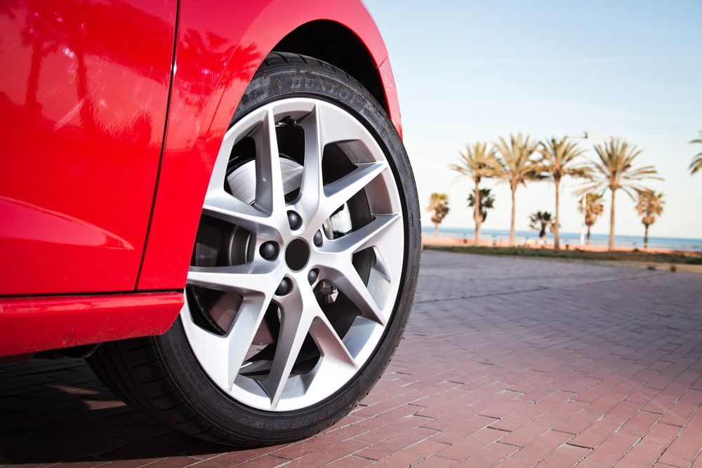 Red Car Wheel on a Brick Road With Palm Trees and Ocean in the Background — Autopro Taree in Taree, NSW