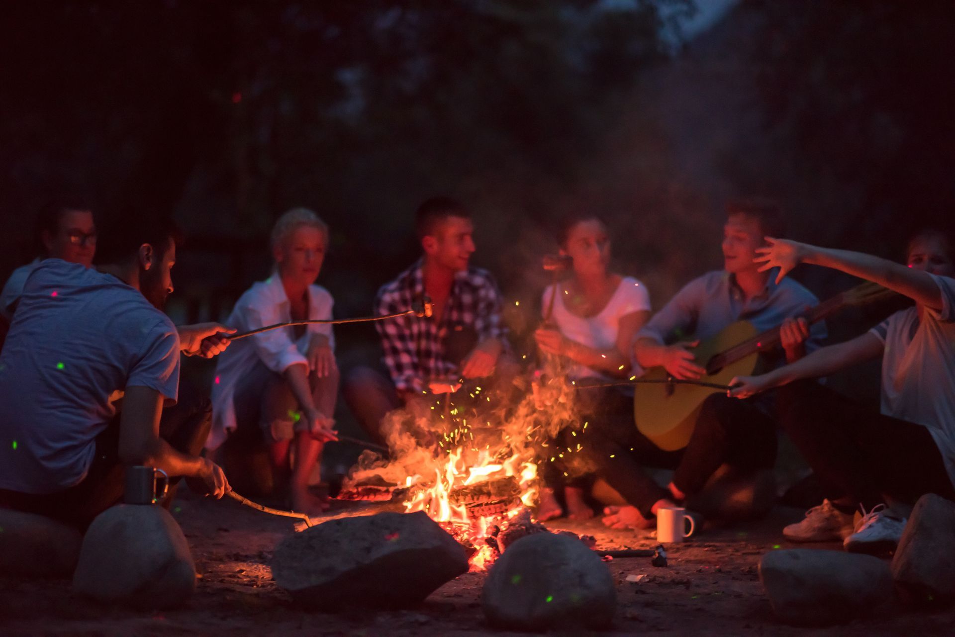 A group of people are sitting around a campfire at night.