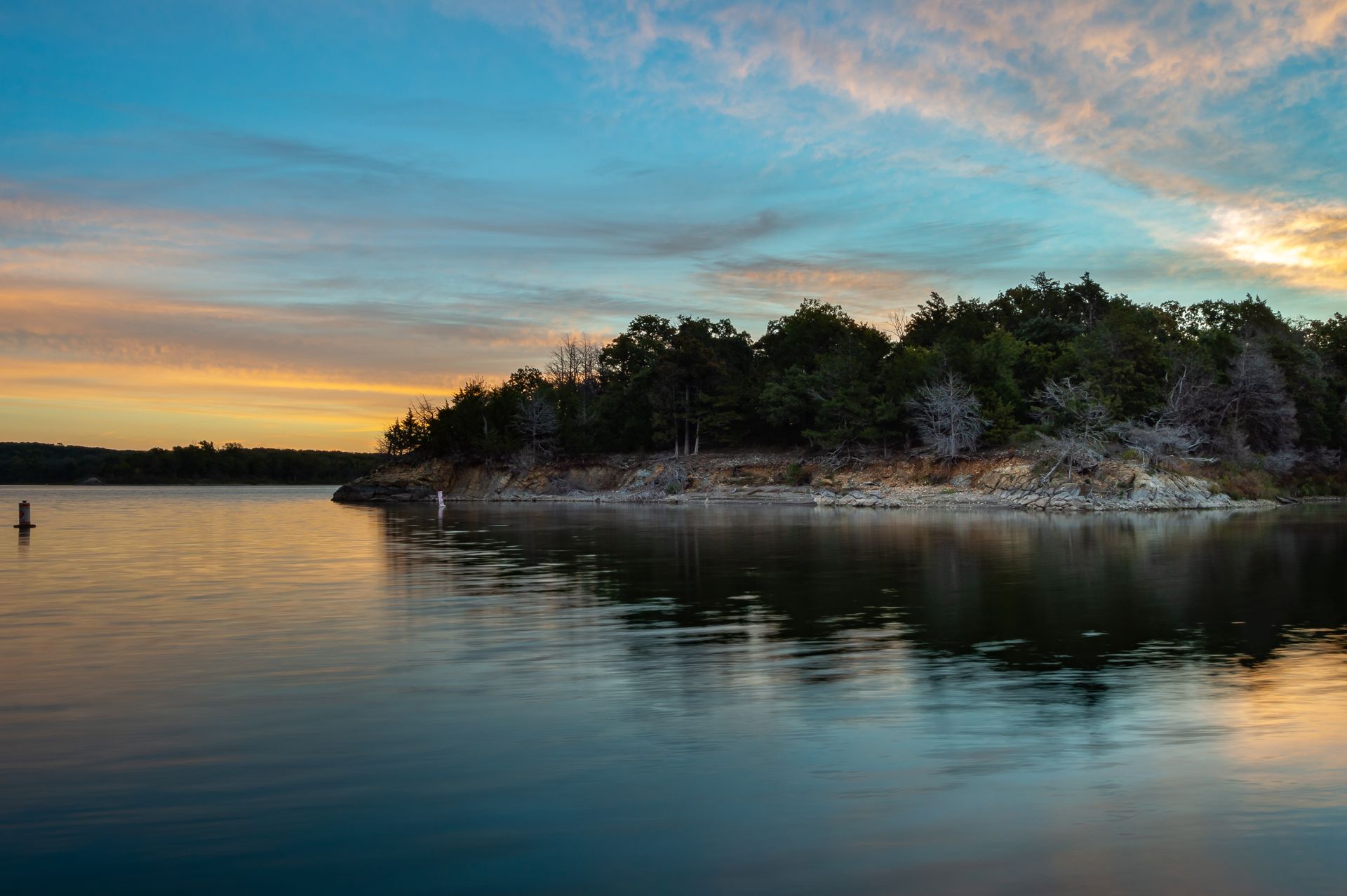 A large body of water with trees on the shore at sunset.