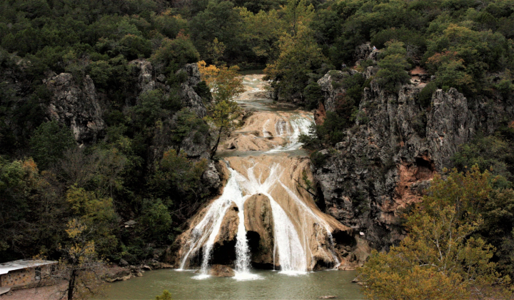 A waterfall is surrounded by trees and rocks in the middle of a forest.