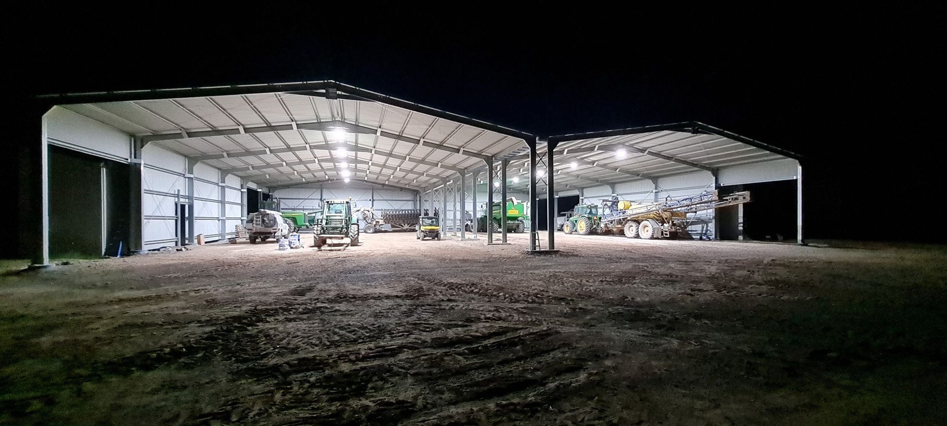 A large warehouse with tractors inside of it is lit up at night.
