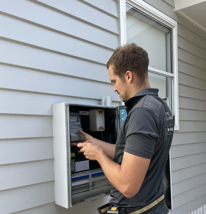 A man is working on an electrical box on the side of a house
