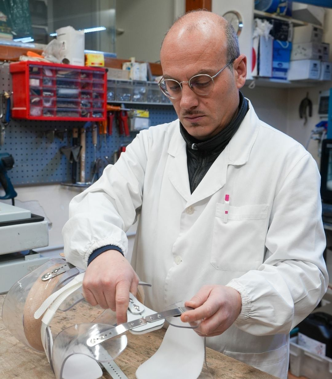 Uomo in camice da laboratorio che regola un dispositivo ortopedico con degli attrezzi in un'officina.