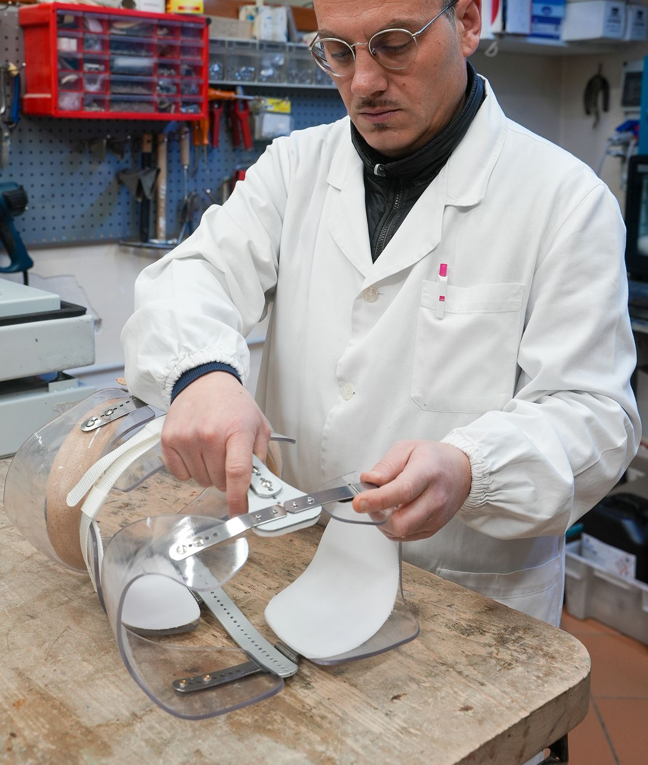 Calzolaio in camice bianco al lavoro su un pezzo di scarpa con gli attrezzi su un banco da lavoro.