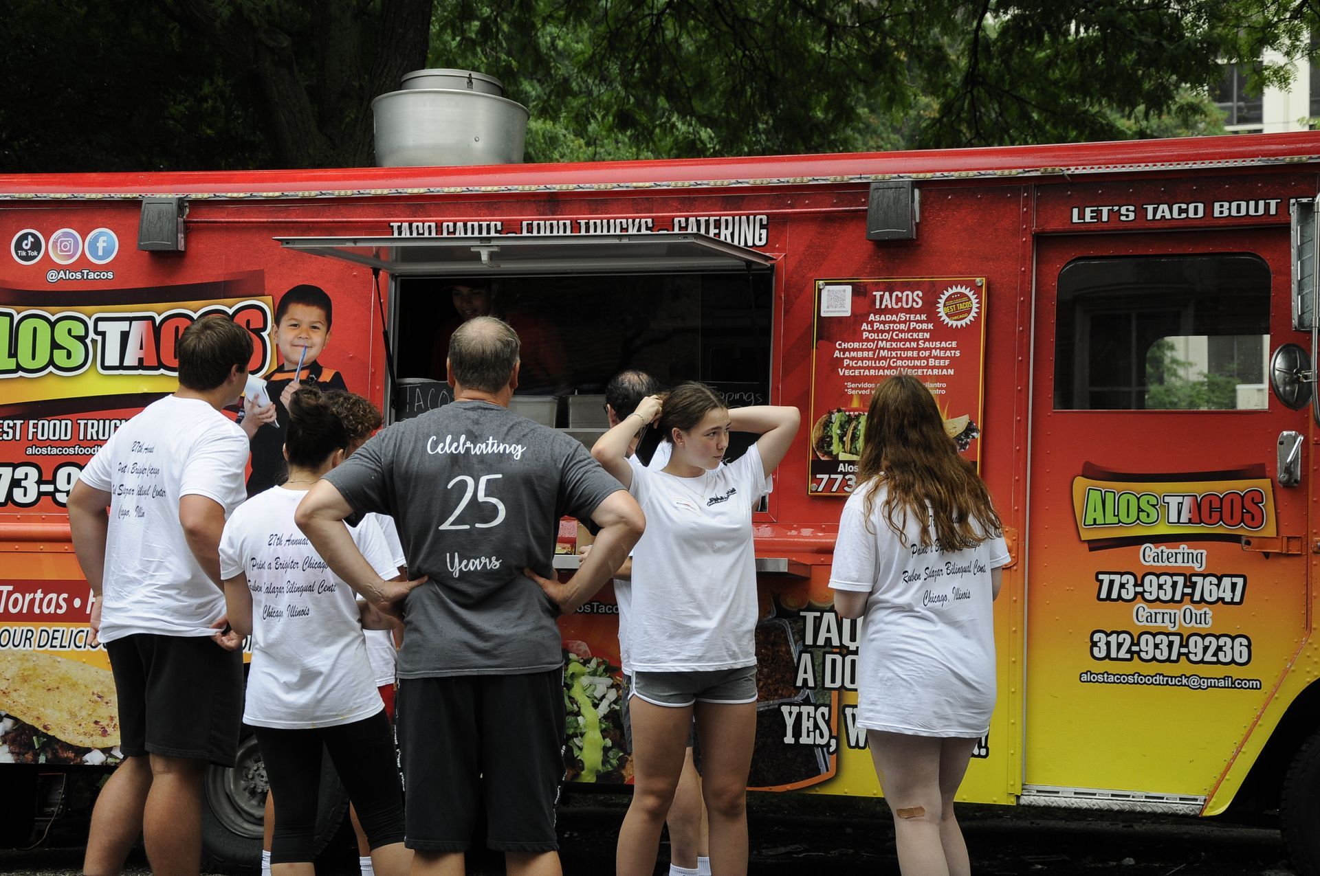 A group of people standing in front of a food truck with the number 25 on the back