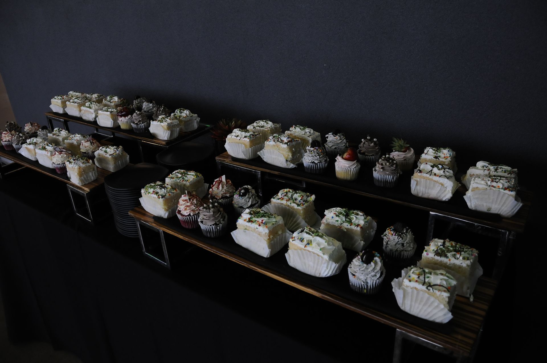 A table filled with lots of cupcakes and cakes in a dark room.