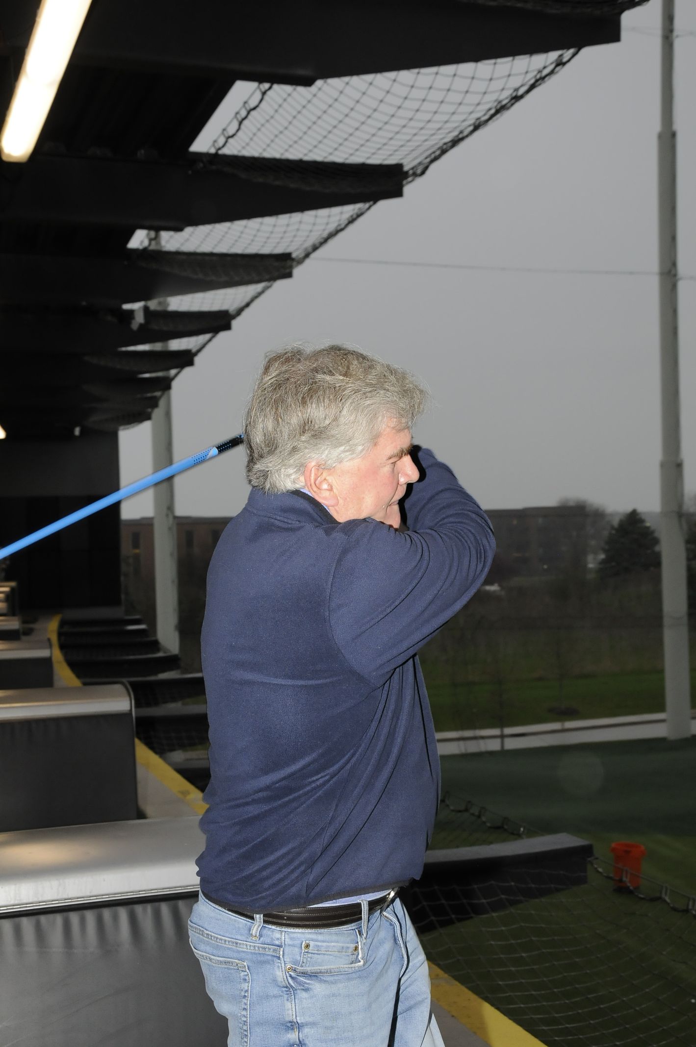 A man in a blue sweater is swinging a golf club