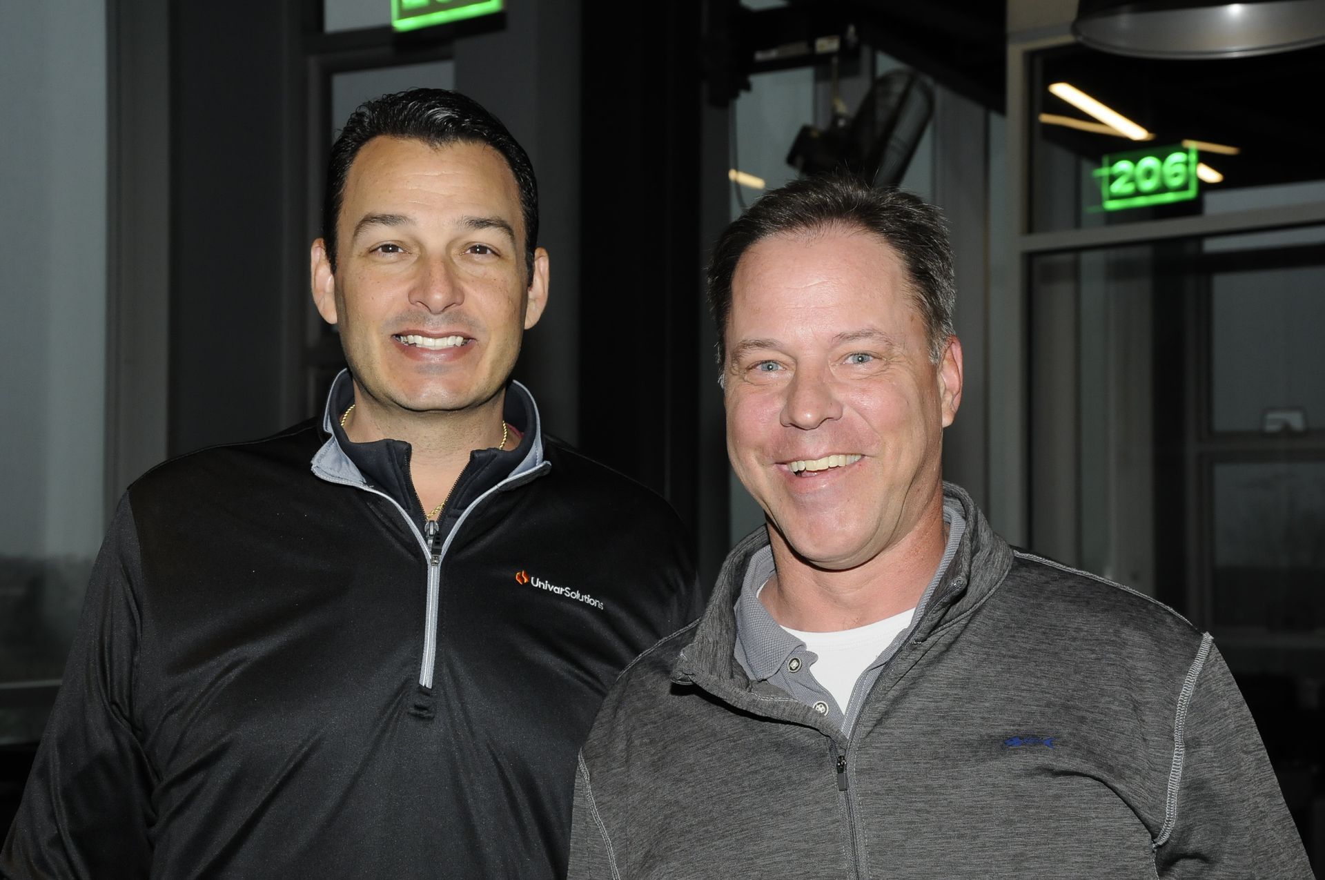 Two men are standing next to each other in front of a green exit sign.
