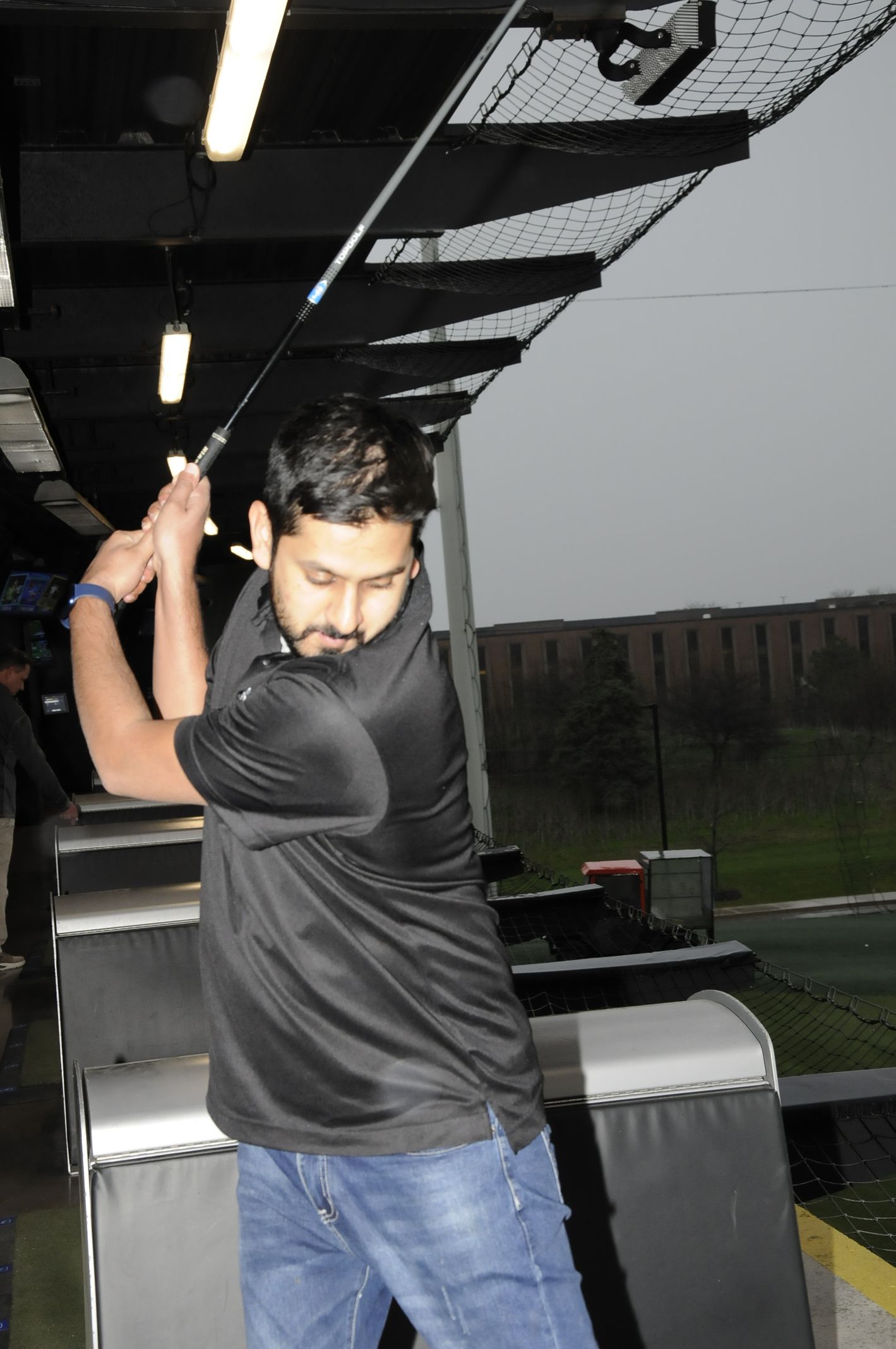 A man in a black shirt is swinging a golf club