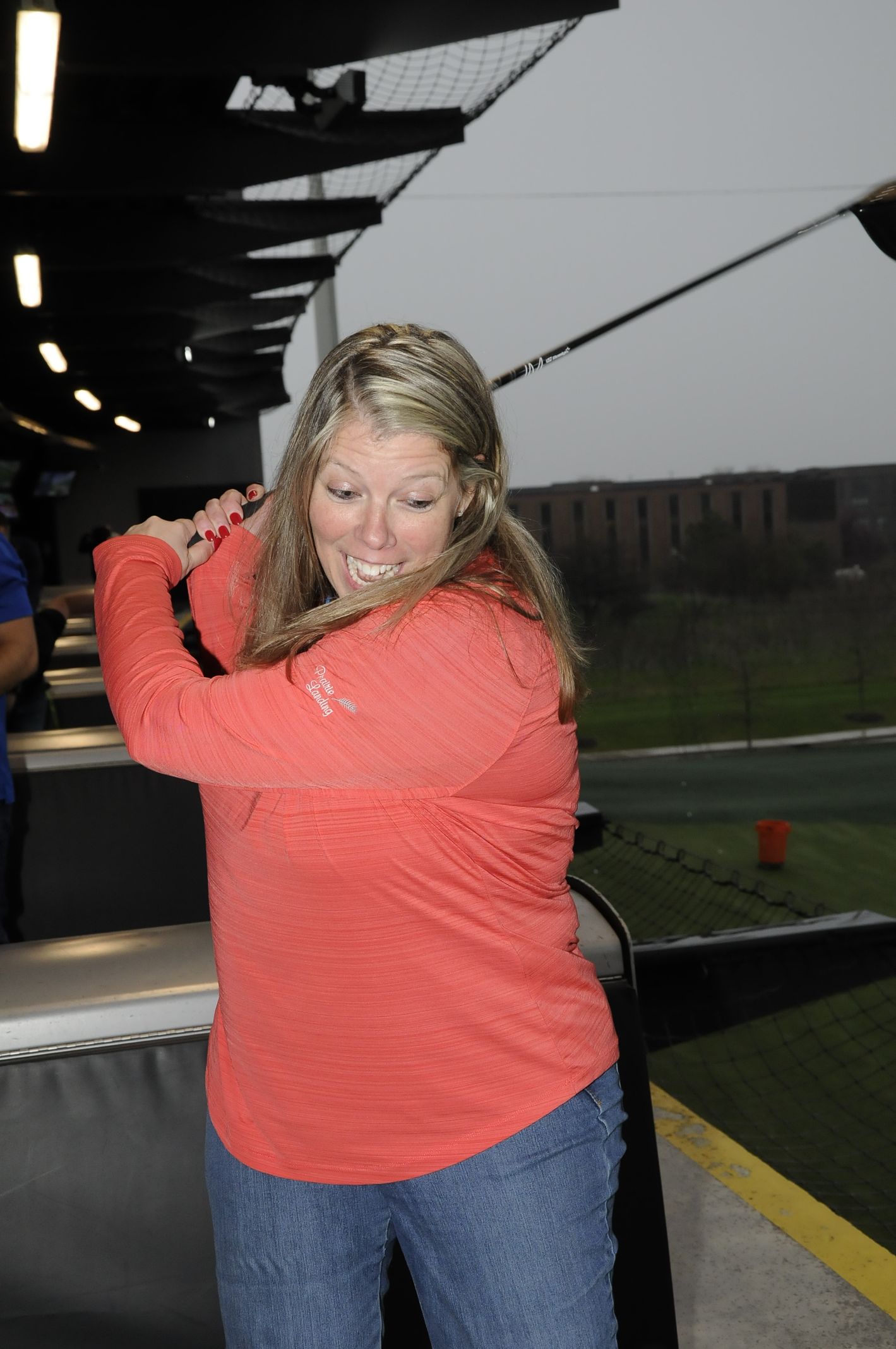 A woman in a red shirt is swinging a golf club