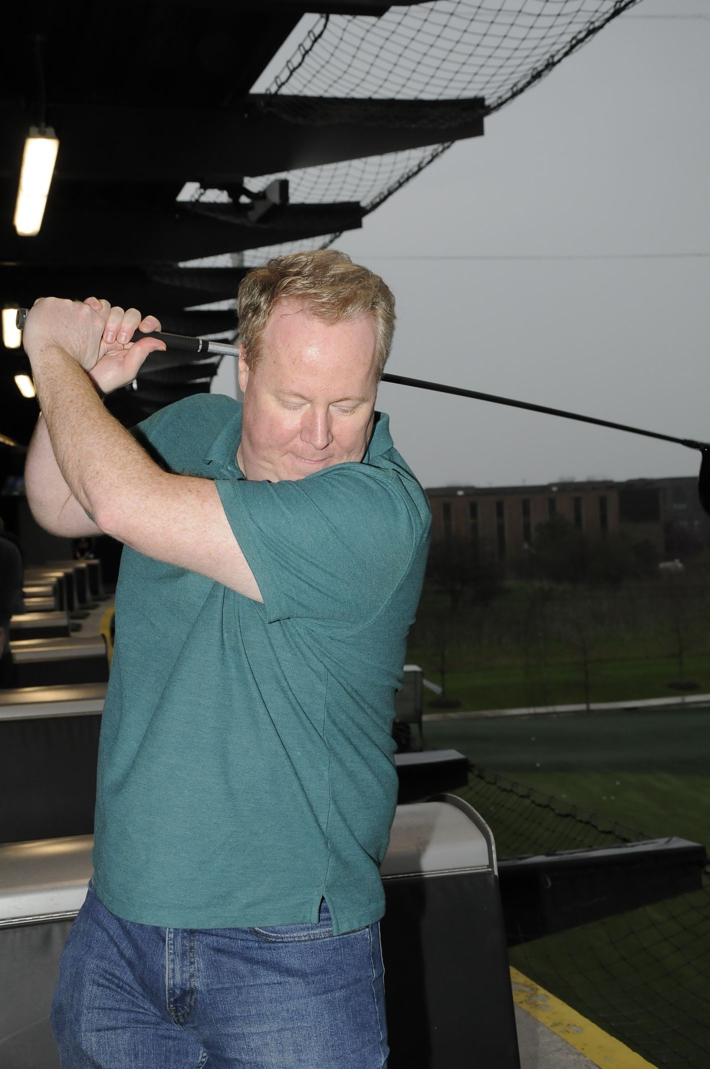 A man in a green shirt is swinging a golf club