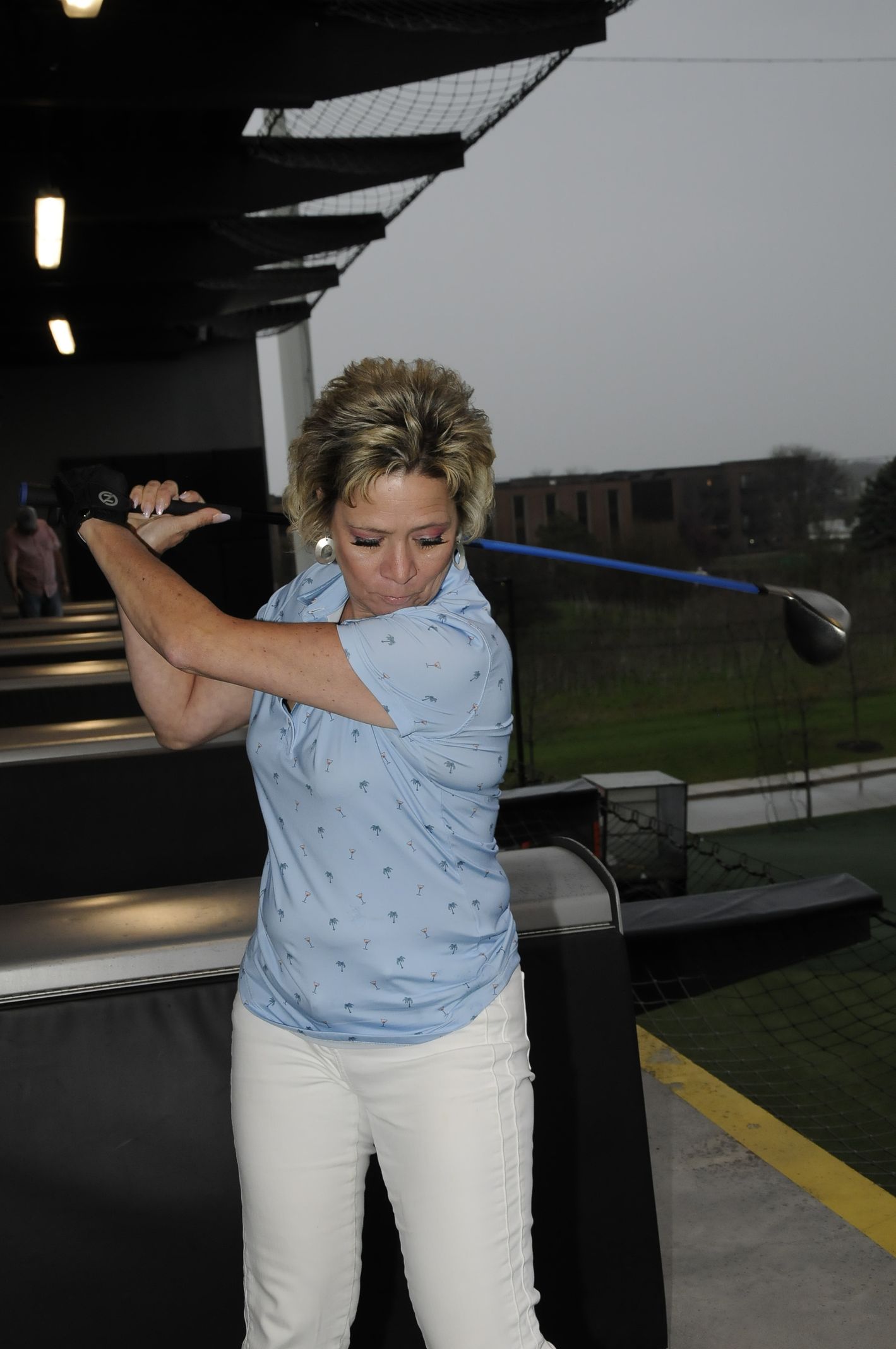 A woman in a blue shirt is swinging a golf club