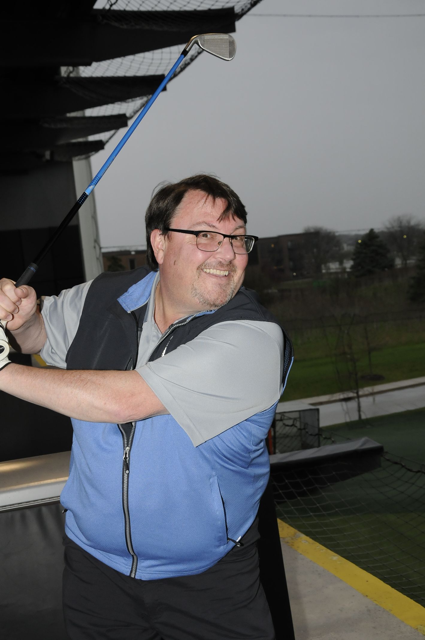 A man in a blue vest is swinging a golf club