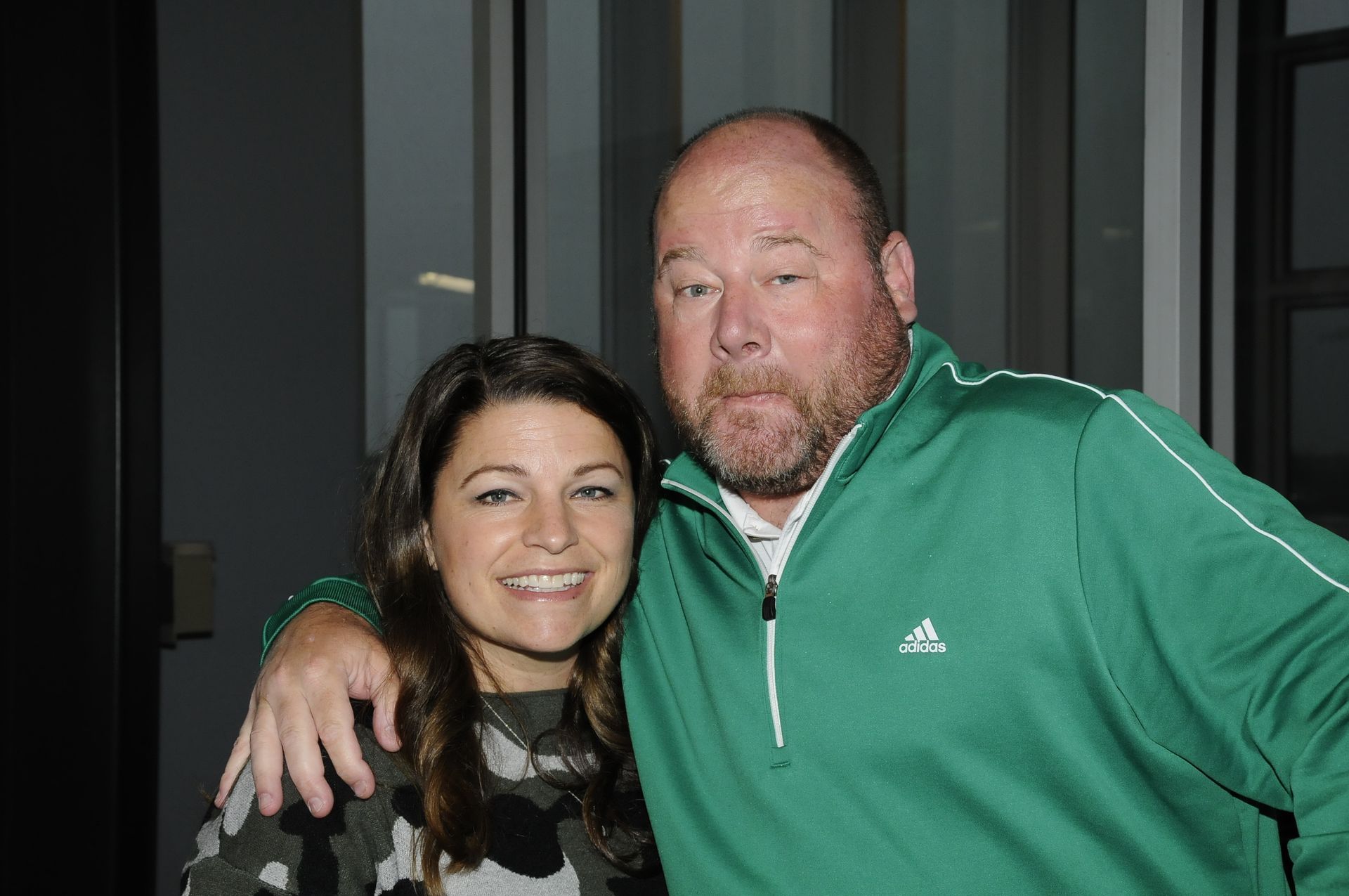 A man in a green adidas jacket is posing for a picture with a woman