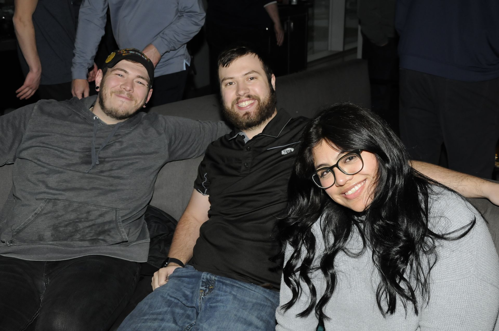 Three people are posing for a picture while sitting on a couch.