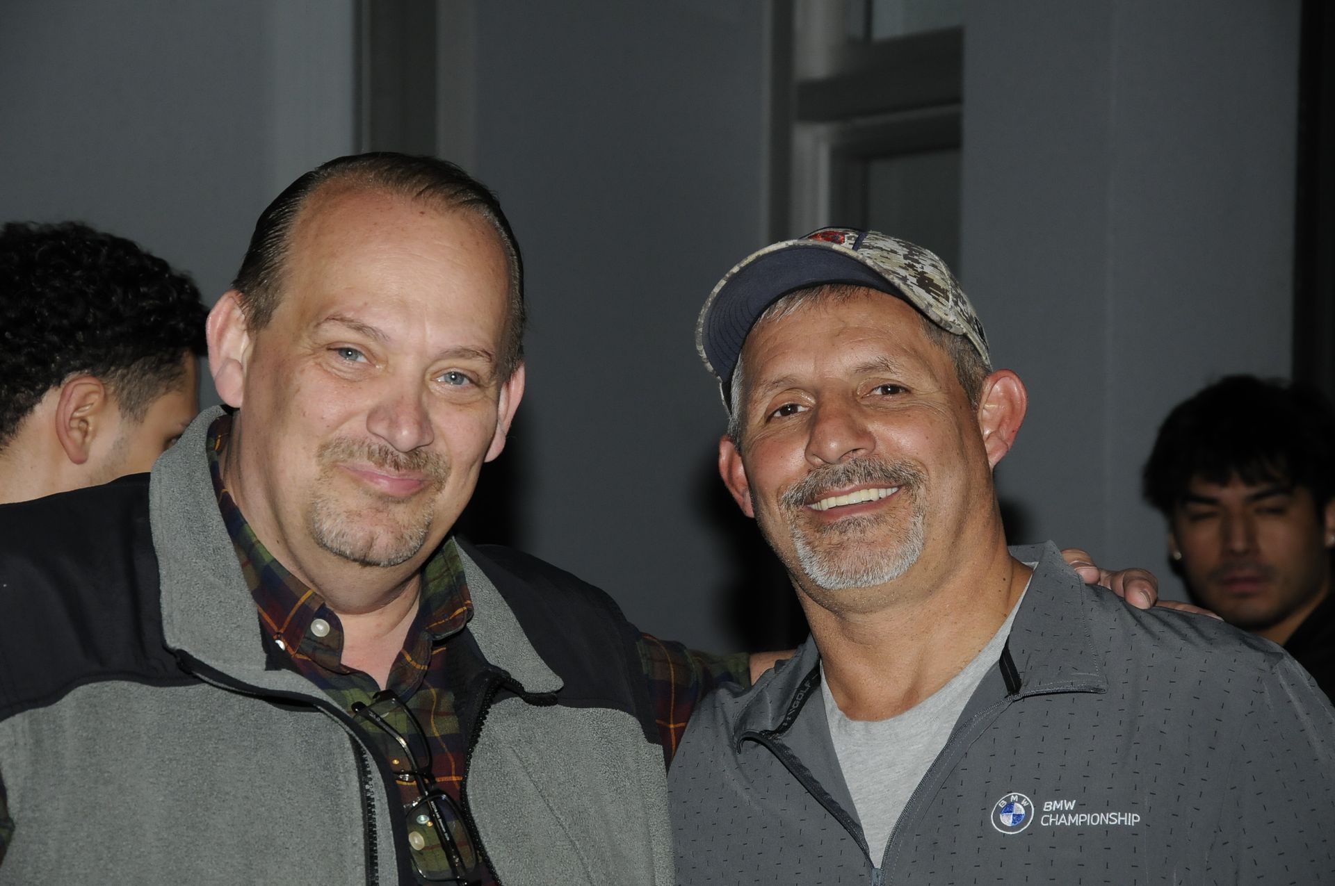 Two men are posing for a picture together and one of them is wearing a hat.