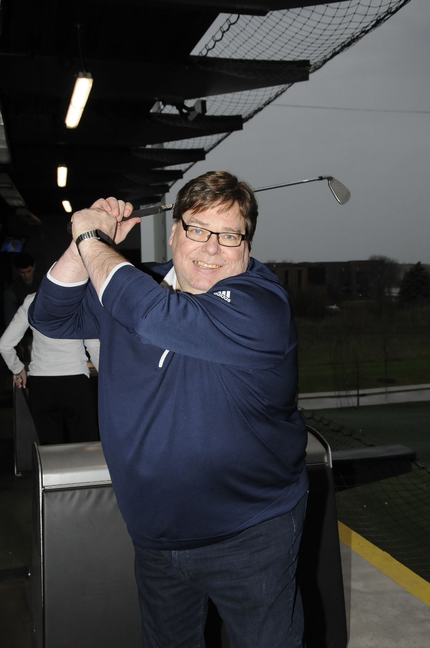 A man wearing glasses is swinging a golf club