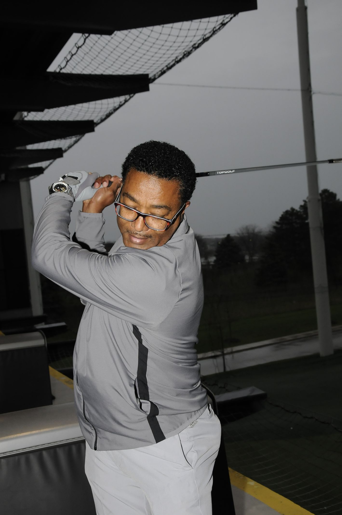 A man wearing glasses is swinging a golf club