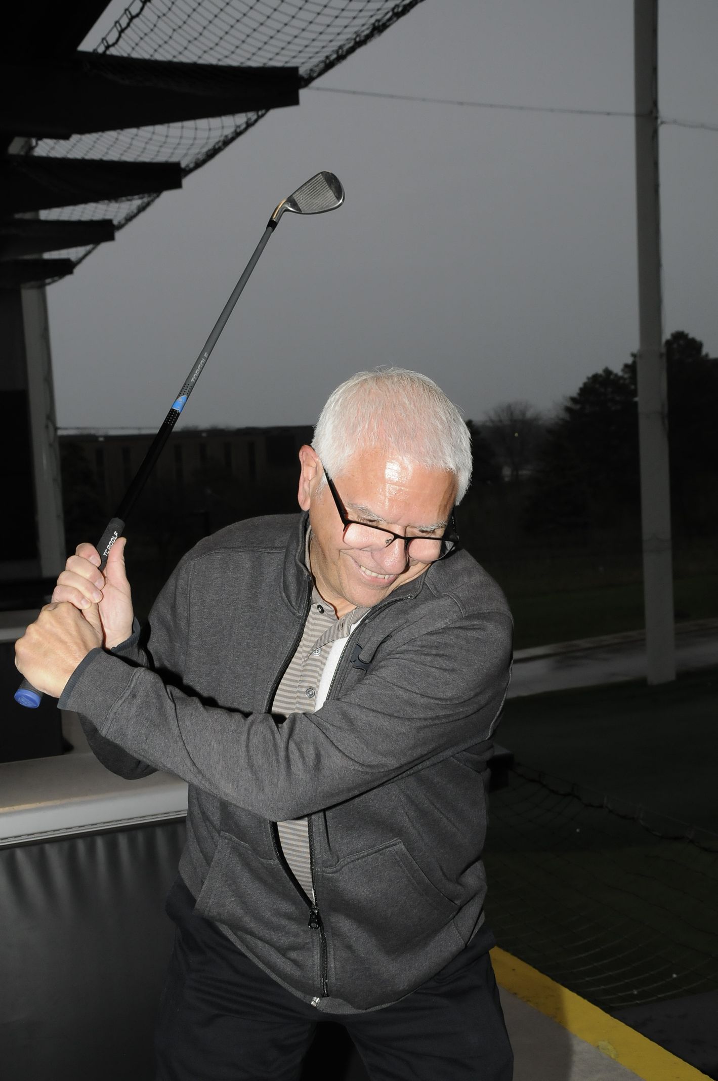 A man wearing glasses is swinging a golf club
