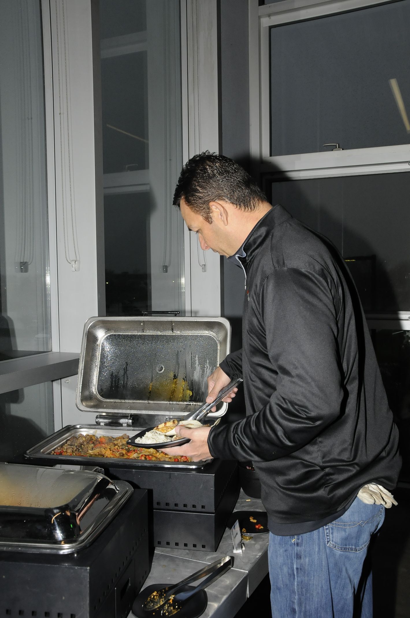 A man in a black jacket is preparing food in a buffet line